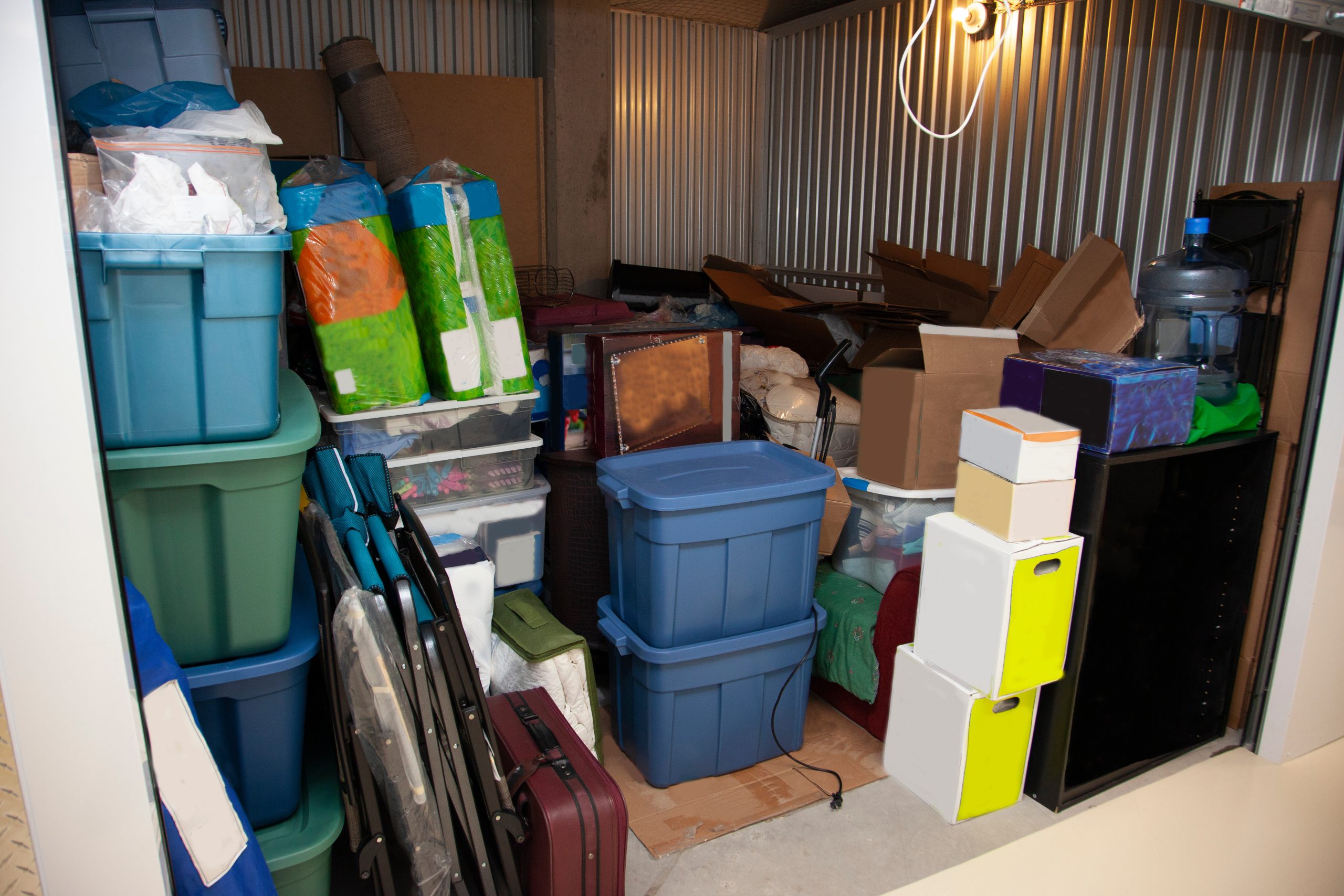 Packed self-storage unit filled with household items, storage bins, boxes, and furniture.
